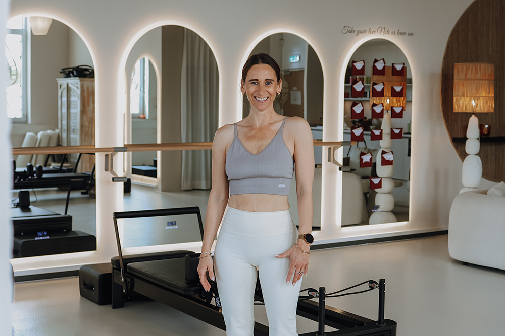 Janett Schmied steht in ihrem Reformer Pilates Studio in Sportkleidung.